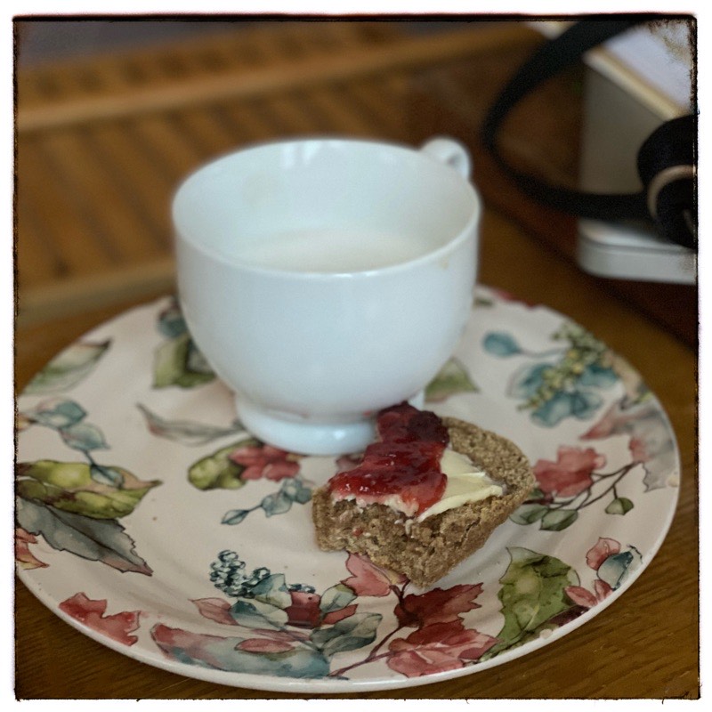cup of coffee with a small portion of a Irish Soda farl with butter and jam on a colourful plate. 