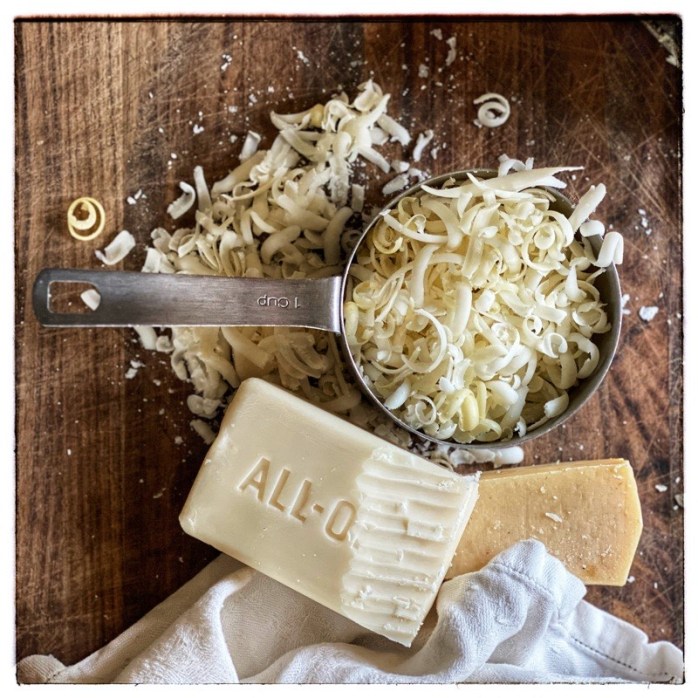 1 cup grated soap in stainless steel measuring cup on wooden surface. Grated soap ready to be made into home made laundry liquid