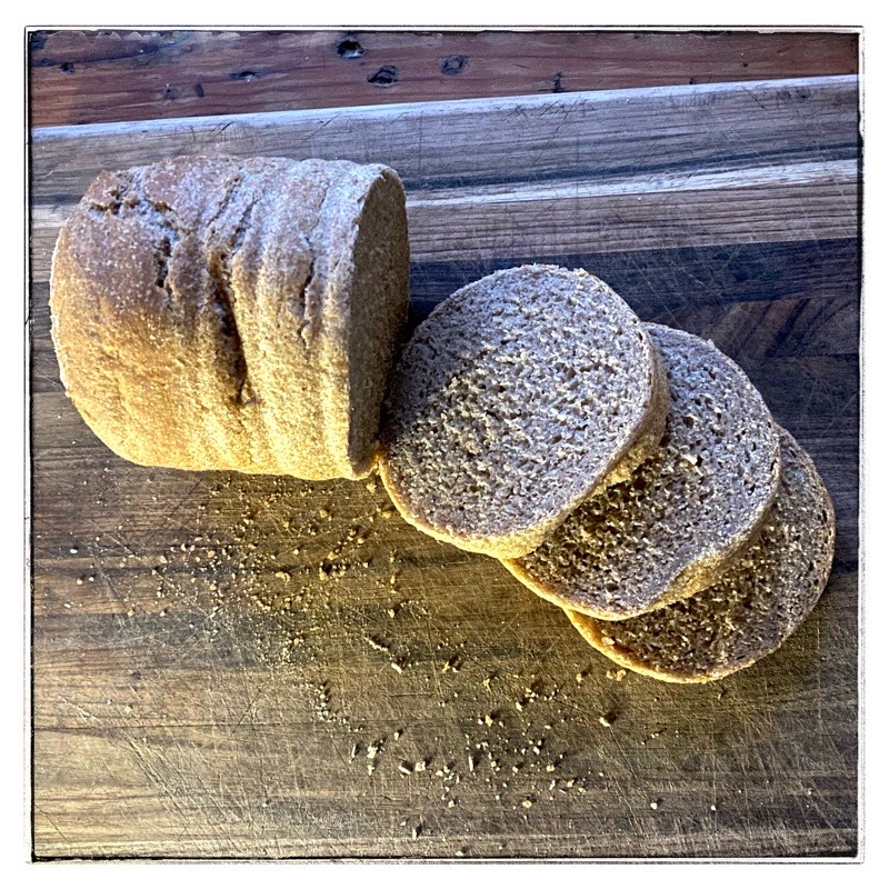 Round loaf of whole meal bread. Three slices cut off. On wooden chopping block. 