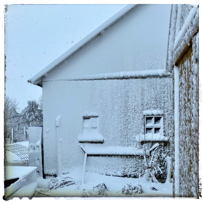 Wet snow attached to side of barn. Windows obscured with snow.  Winter buildings. 