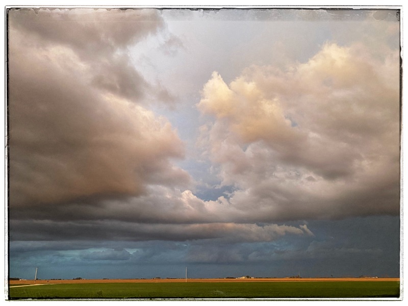 Storm clouds in the West pinkened by the sunset in the East. Above fields on the plains.