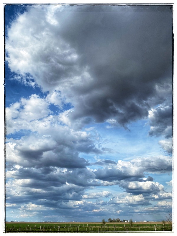 Midwest sky. Midwest clouds. Flat country. Cow fields with fences in the foreground. Grey and white clouds above. 