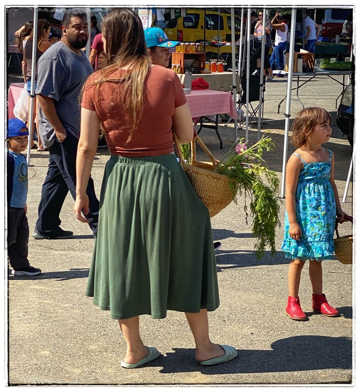 Woman with basket of vegetables  and child. At the farmers market. 