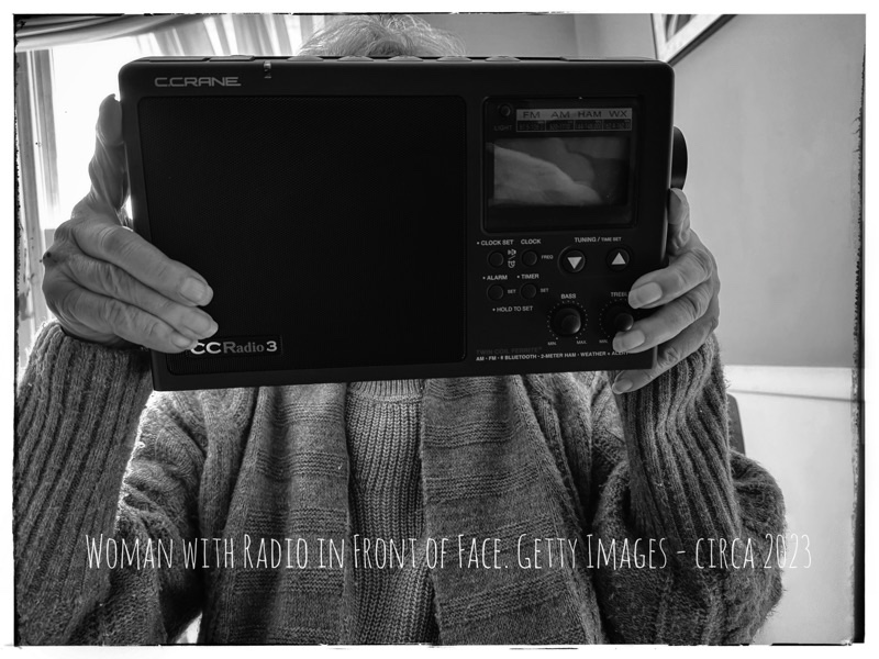 Black and white photograph. Old lady with radio held up in front of her face. 