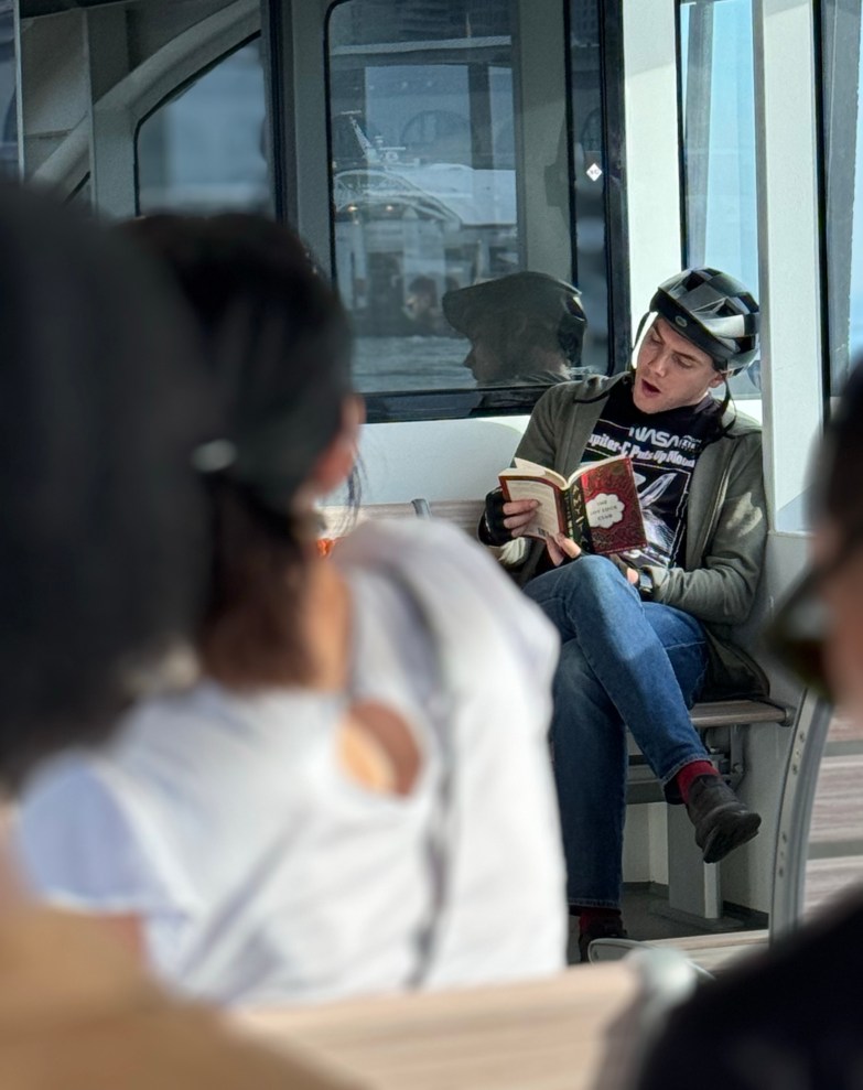 Young man in bicycle helmet reading book on ferry 
