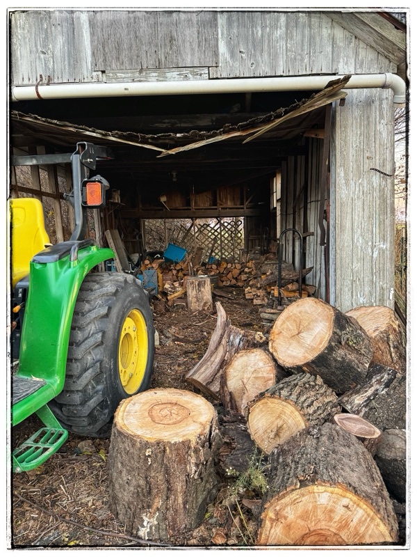 Firewood in wood shed with blue splitter attached to John Deere tractor 