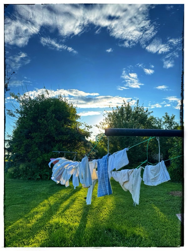 Tea towels, and washcloths drying on a clothesline outside, under a blue sky with clouds