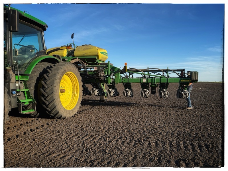 John Deere tractor with planting arm in open field blue sky above 